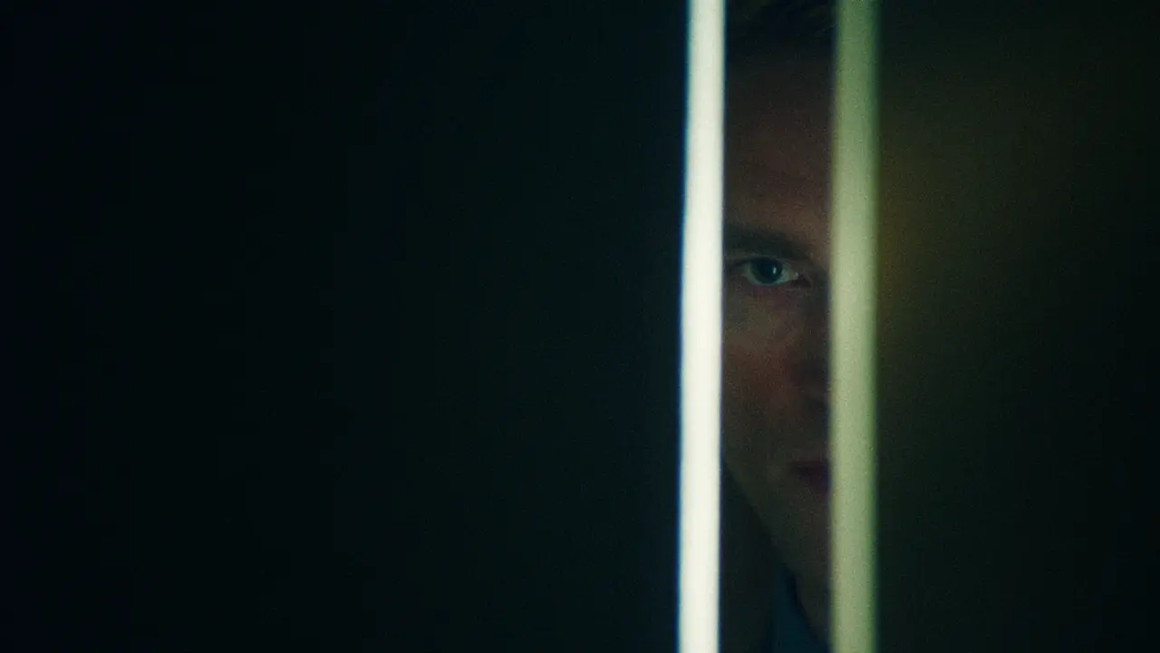 Teaser still — a face half-lit through a cracked doorway.